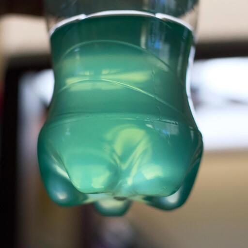 A partially fillled plastic bottle of Baja Blast with the background gently out of focus. The soda is glowing with a blue green light from the sun